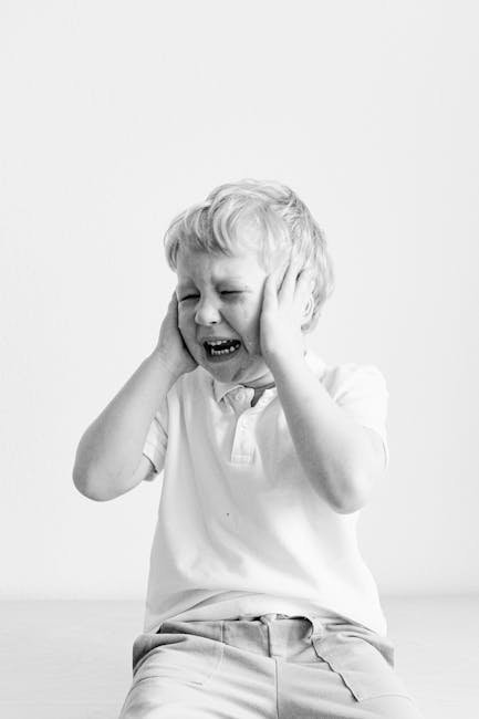 Black and white portrait of a sad child covering ears, expressing frustration.